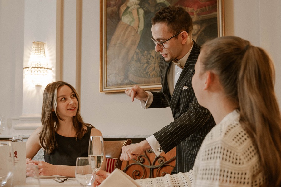 Ein Kellner spricht mit zwei Gästen in einem feinen Restaurant während des Essens.